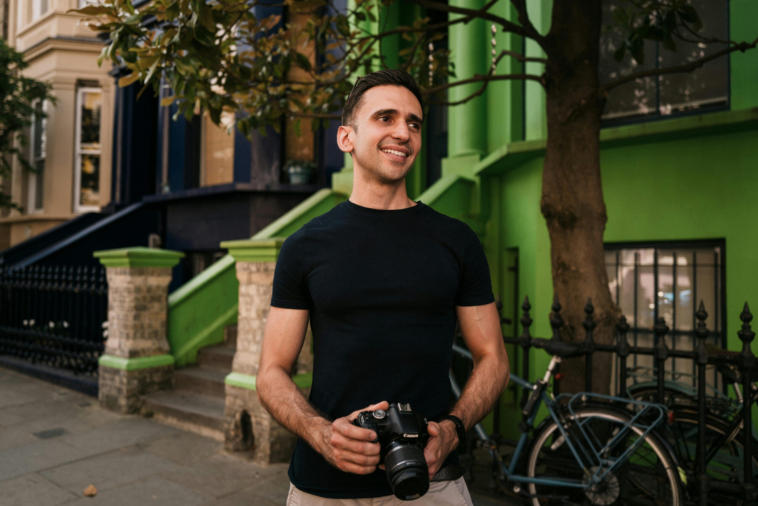 A cheerful photographer holding a camera, captured on a colorful London street.